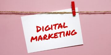 Sticker with the inscription digital marketing hanging on a rope on a pink background